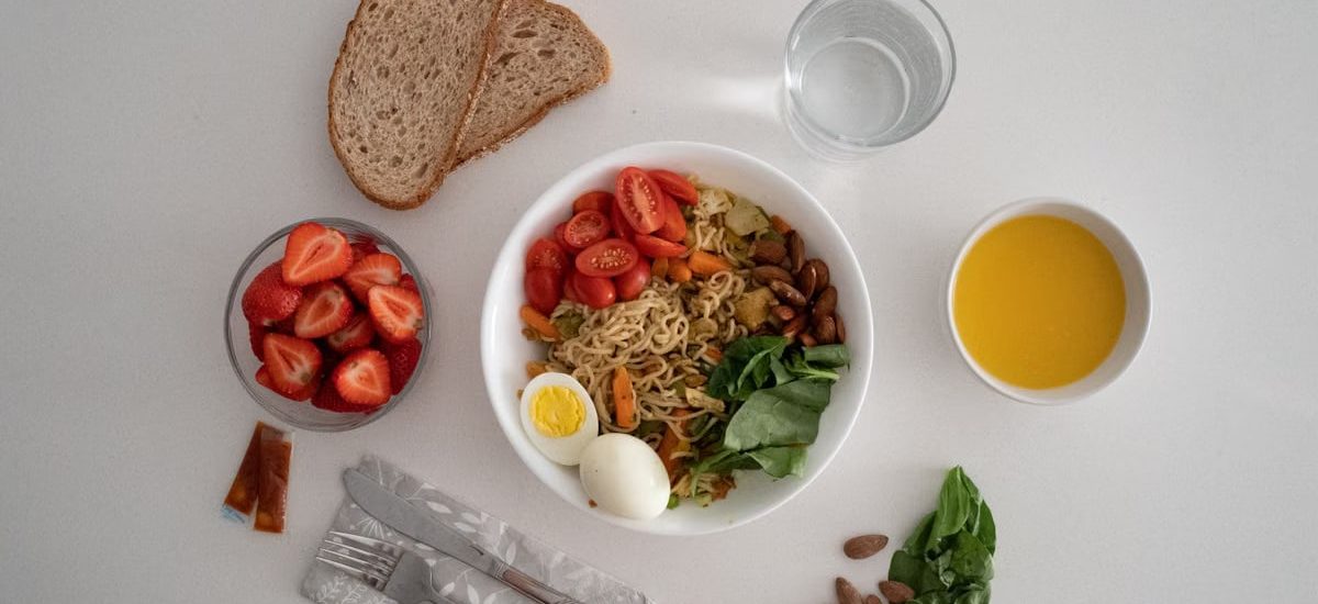 A balanced meal featuring a variety of healthy ingredients including noodles, eggs, almonds, strawberries, and fresh vegetables.
