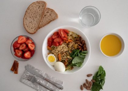 A balanced meal featuring a variety of healthy ingredients including noodles, eggs, almonds, strawberries, and fresh vegetables.