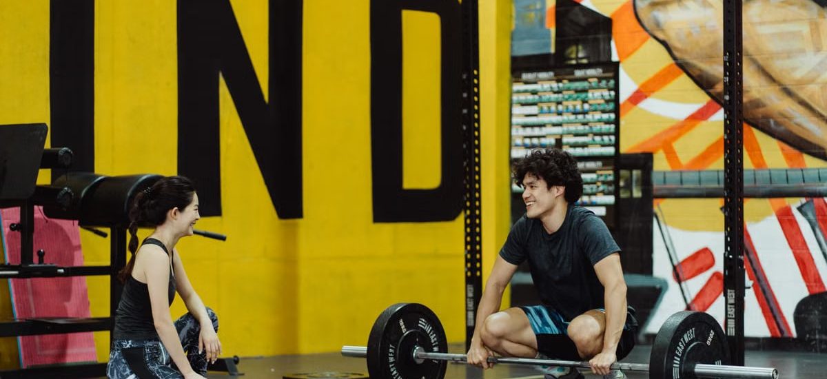 Two young adults in a gym participating in a weightlifting session, sharing a positive moment.